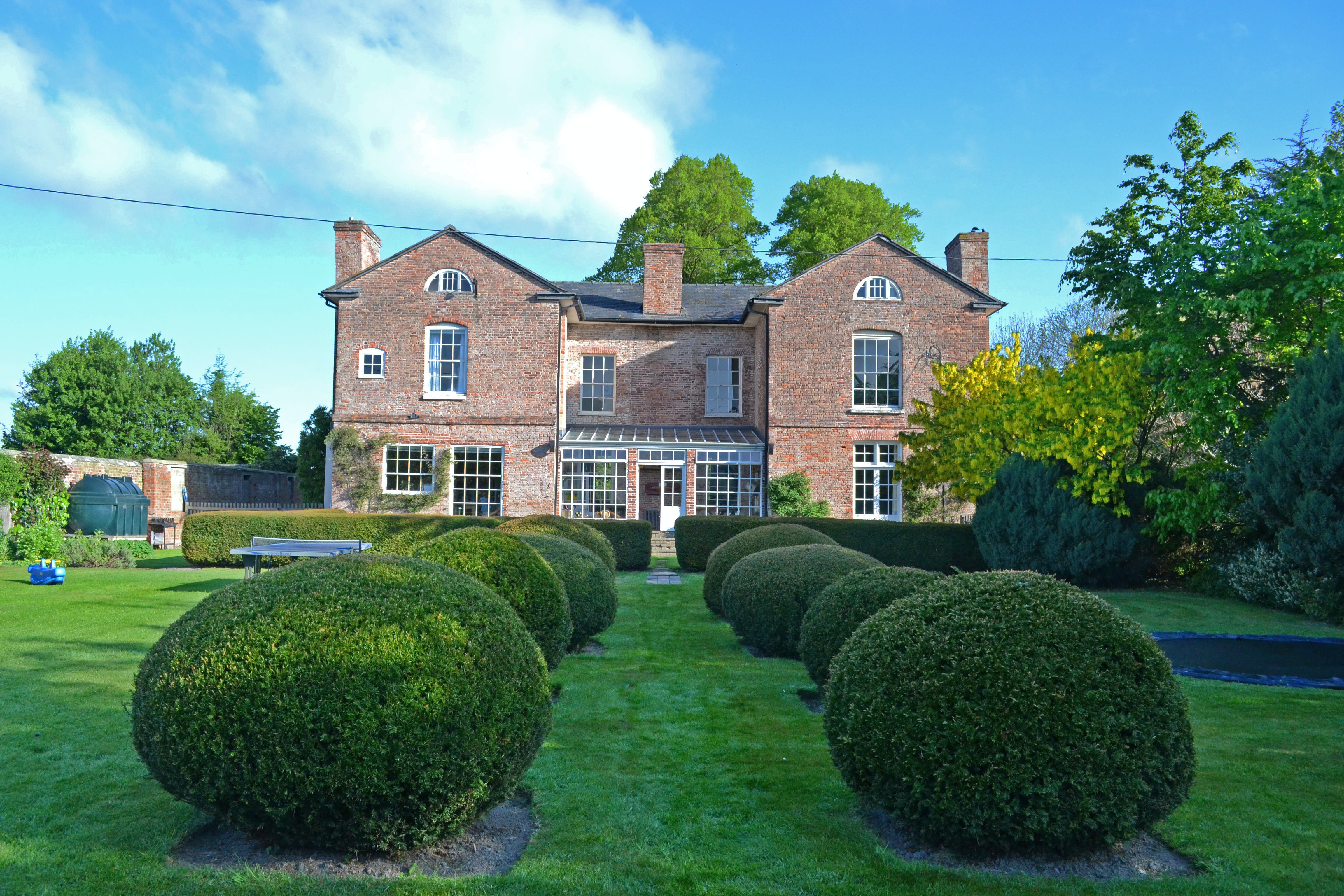 a large brick house with a lawn and hedges in front of it with Moseley Old Hall in the background